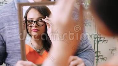 年轻女子在<strong>眼镜店</strong>用镜子检查她的新眼镜。 戴眼镜的年轻女子